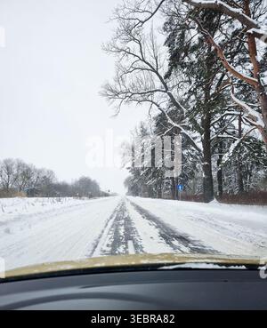Fahren auf einer verschneiten Straße durch einen Winterwald. Aus der Perspektive der ersten Person aus dem Armaturenbrett des Fahrzeugs auf einer vereisten, schneebedeckten Asphaltstraße. Stockfoto