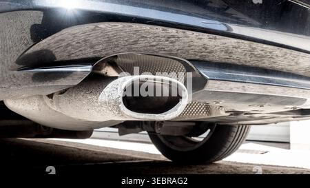 Nahaufnahme eines Pkw-Auspuffrohrs und Schalldämpfers unter dem hinteren Stoßfänger - CO2-Emissionen und Abgasverschmutzung durch Verbrennungsfahrzeuge Stockfoto