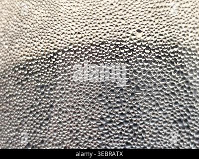 Nahaufnahme von Wassertröpfchen auf der Glasoberfläche mit Kondensationstextur, die ein dichtes Feuchtigkeitsmuster auf weichem, verschwommenem Hintergrund bilden. Stockfoto