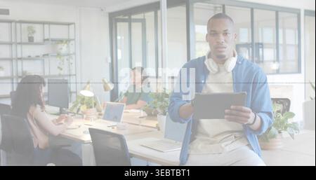 Tablet halten, Kopfhörer tragen, Mann mit beigefarbenem Hemd auf dem Schreibtisch im Büro, Kopierraum Stockfoto