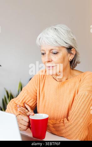 Ältere Frau hört Kollegen während der Arbeit von zu Hause aus auf einem Laptop-Videoanruf zu Stockfoto