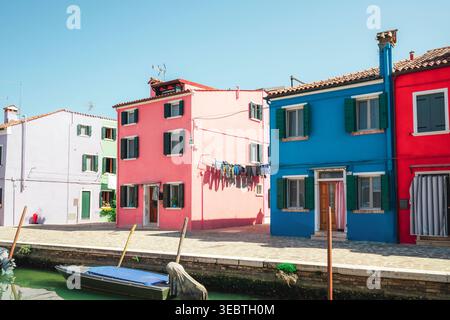 Farbenfrohe Häuser entlang des Kanals auf der Insel Burano, Venedig, Italien mit hellen Fassaden und kleinen Booten unter klarem blauem Himmel. Stockfoto