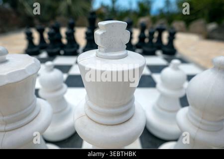 Eine Nahansicht eines großen Schachspiels im Freien, der den weißen König im Vordergrund auf einem karierten Brett zeigt. Stockfoto
