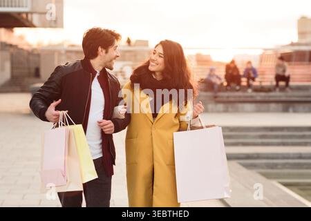 Paare genießen Shopping und Spaziergänge in der Stadt während Sonnenuntergang mit Taschen in der Hand Stockfoto