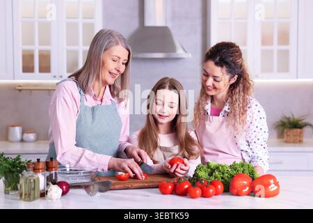 Glückliche Großmutter, ihre Tochter und Enkelin kochen zusammen am Tisch in der Küche Stockfoto