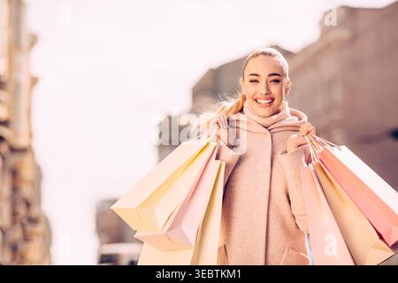 Frau genießt Shopping an einem sonnigen Tag in einem lebhaften Stadtgebiet mit festlichen Taschen Stockfoto