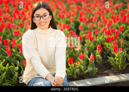 Junge Frau lächelt in einem Feld aus roten Tulpen während des sonnigen Frühlingnachmittags Stockfoto