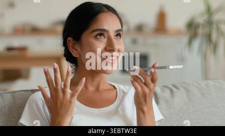 Glückliche aufgeregte arabische indische Frau, die Audio-Nachricht Voicemail zu Hause aufnimmt sprechendes Mikrofon auf Handy weibliches Mädchen jubelt mit Stockfoto