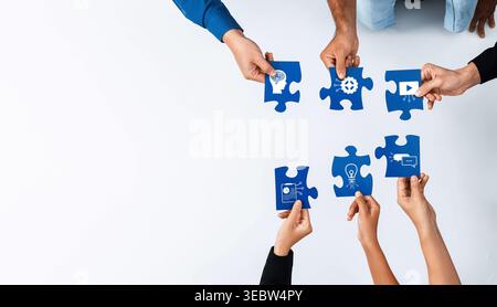 Dieses Bild zeigt eine gemeinsame Arbeit, bei der verschiedene Hände zusammenkommen, um Puzzleteile zusammenzustellen und Teamarbeit, Kreativität und gemeinsame Lösungen zu symbolisieren Stockfoto