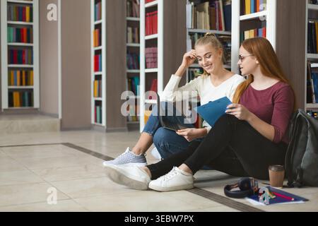 Freunde studieren gemeinsam in einer Bibliothek, während sie tagsüber auf dem Boden sitzen Stockfoto
