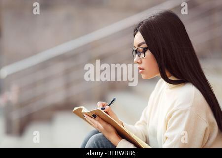 Junge Frau, die im Notizbuch während der Lernsitzung im stillen Innenraum schreibt Stockfoto