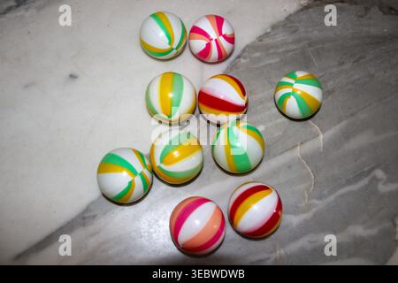 Ein Blick von oben auf zehn kleine, federnde Gummikugeln mit bunten Drallmustern, die locker auf einer grauen Tischplatte aus poliertem Marmor angeordnet sind. Stockfoto