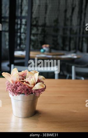Eine detaillierte Nahaufnahme einer eleganten pfirsichfarbenen Cymbidium-Orchideenblume, gemischt mit kleinen rosafarbenen Knospen, präsentiert in einem kleinen Rost Stockfoto