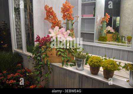 Eine bezaubernde Indoor-Szene mit rustikalem Blumendesign auf einem weißen Sideboard aus Holz. Die Hauptanordnung umfasst rosa Lilien, kastanienbraune Orchideen, Stockfoto