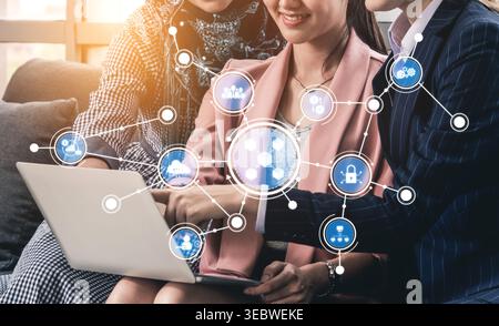 Drei verschiedene Fachleute führen eine gemeinsame Diskussion über ein Notebook, umgeben von digitalen Symbolen, die Technologie, Netzwerke und veranschaulichen Stockfoto