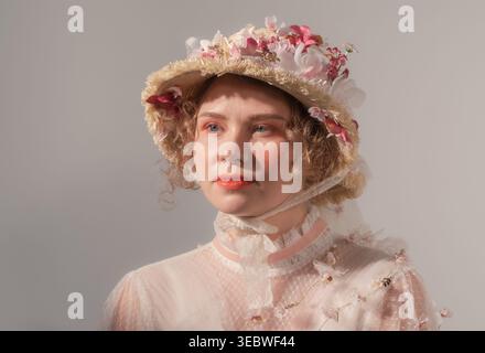 Die Models junger Frauen haben einen raffinierten Blumenhut und ein transparentes, im Vintage-Stil inspiriertes Oberteil in einem hellen Studio Stockfoto