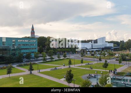 HELSINKI, FINNLAND - 11. AUGUST 2025: Erhöhter Blick auf einen öffentlichen Park und Bürgerhäuser mit Kirchturm unter teilweise bewölktem Himmel. Stockfoto