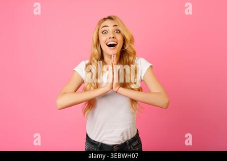 Aufgeregte junge Frau mit langen blonden Haaren, die Freude vor rosafarbenem Hintergrund ausdrückt Stockfoto