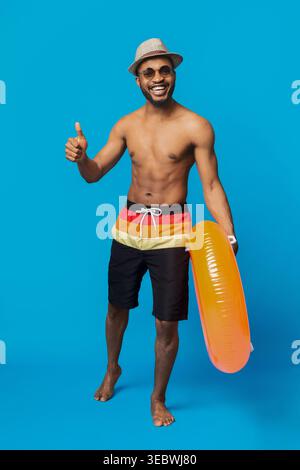 Junger Mann, der den Sommer mit Orange Float und Strandkleidung vor einem lebhaften blauen Hintergrund genießt Stockfoto