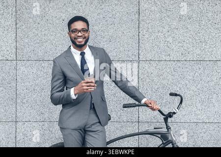 Junger Profi im Anzug, der Kaffee genießt, während er sich in urbaner Umgebung gegen das Fahrrad lehnt Stockfoto