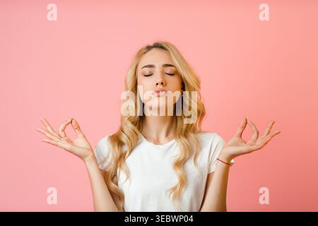 Junge Frau, die Achtsamkeit und Meditation in einer ruhigen Umgebung mit rosafarbenem Hintergrund übt Stockfoto
