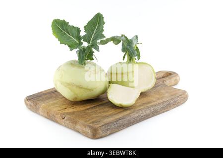 Zwei ganze Kohlrabi-Zwiebeln und eine Scheibe werden auf einem strukturierten Holzbrett vor einem sauberen weißen Hintergrund präsentiert, wodurch ihre klare Textur und V hervorgehoben werden Stockfoto