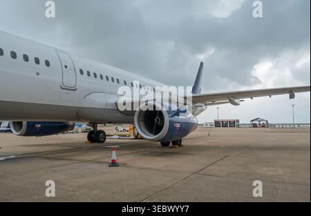 Weißer kommerzieller Jetliner parkt auf dem Flughafenvorfeld mit blauem Motor gegen graue Wolken Stockfoto
