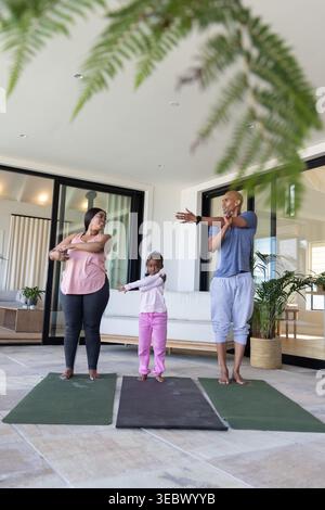 Afroamerikanische Familie in Trainingskleidung, die sich auf der Terrasse mit Yogamatten und Fitness-Tracker ausdehnt Stockfoto