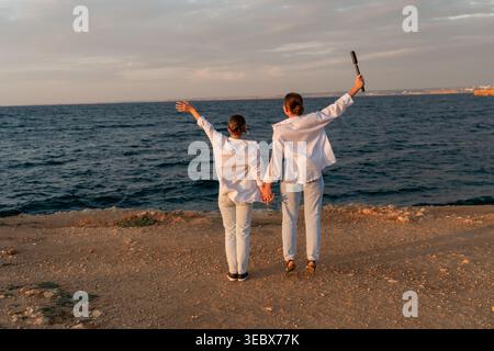 Paare Beach Sunset Celebration - Ein Paar, Das die Hände hält, hebt die Arme in die Luft, während es einen Sonnenuntergang am Strand feiert. Stockfoto
