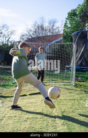 Jungs spielen Fußball in einem Garten, einer tritt den Ball in Richtung Tor Stockfoto