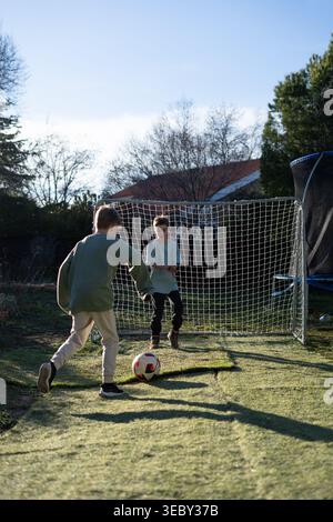 Jungen spielen im Freien und haben tagsüber Spaß, den Ball in Richtung Tor zu treten Stockfoto