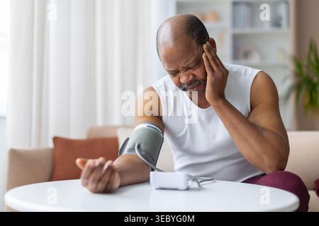 Ein gereifter schwarzer Mann mit Blutdruckmanschette und berührendem Kopf Stockfoto