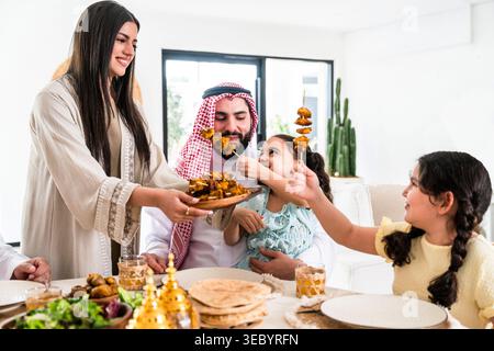 Arabische Eltern und Kinder teilen sich zu Hause eine Mahlzeit, die Mutter serviert Essen und eine Tochter füttert Döner an ihren Vater, was Familienbonbon symbolisiert Stockfoto