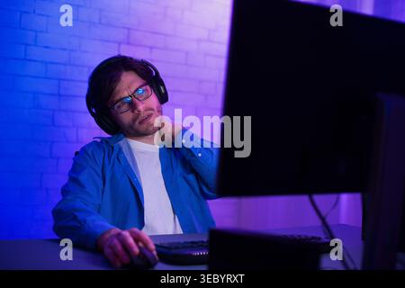 Junger Mann, der den Computer benutzt, während er Kopfhörer trägt und nachdenklich auf den Bildschirm schaut Stockfoto