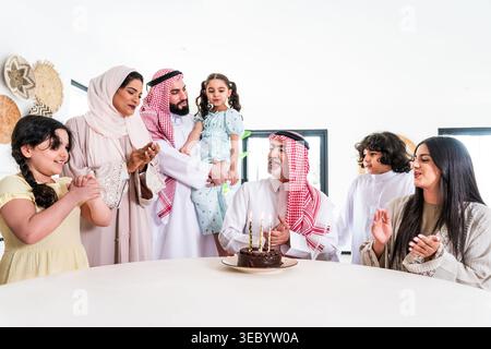 Eine mehrgenerationenübergreifende arabische Familie feiert zu Hause einen Geburtstag, versammelt sich um einen Schokoladenkuchen mit zündeten Kerzen, erzählt freudige Momente der Tradition, Stockfoto