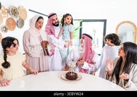 Arabische Großfamilien treffen sich zu Hause an einem Tisch, feiern einen Geburtstag mit einem Schokoladenkuchen, klatschen und genießen den glücklichen Familienmoment Stockfoto