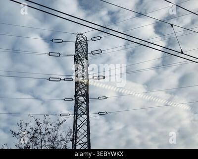 Ein Elektrizitätspylon mit mehreren Kabeln, die über die Kabel gestreckt sind, mit detaillierten Isolatoren, die die Kabel sichern, vor einem dramatischen bewölkten Himmel, dargestellt in Stockfoto