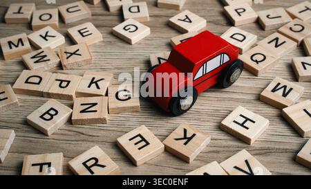 Kleiner roter Holzspielzeugwagen, der sich durch ein Feld aus verstreuten Alphabetfliesen auf einer Holzoberfläche bewegt. Stockfoto