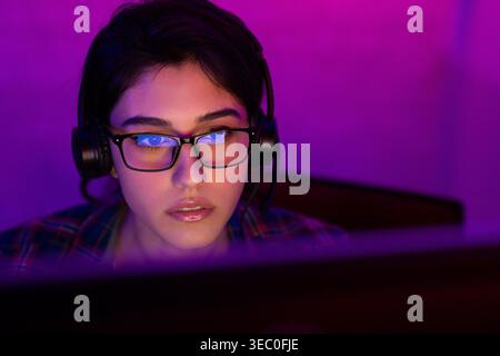 Fokussierte junge Frau, die spät nachts an einem Computer mit Kopfhörern arbeitet Stockfoto