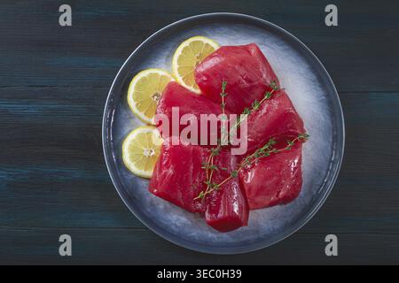 Frische Thunfischstücke werden ordentlich auf einem grauen Teller angeordnet. Zitronenscheiben und Kräuterzweige werden neben den Fisch gelegt Stockfoto