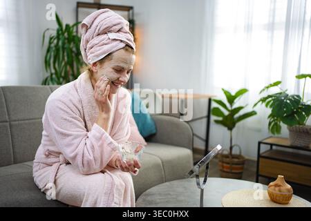 Eine junge Frau, die zu Hause eine Gesichtsmaske aufträgt Stockfoto