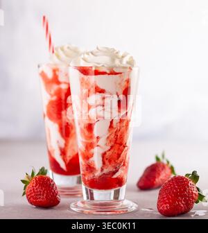 Erdbeermilkshake mit Schlagsahne und Beerensirup im hohen Glas auf hellem Hintergrund. Stockfoto