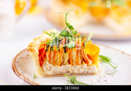 Hausgemachte Gemüsetorte mit Karotten, Zucchini und Kürbis auf einem weißen Holztisch. Spiralförmige Gemüsetorte. Stockfoto
