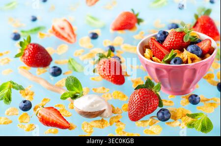 Konzept eines gesunden glutenfreien Frühstücks mit Beeren, natürlichem Joghurt und Cornflakes auf blauem Hintergrund. Stockfoto