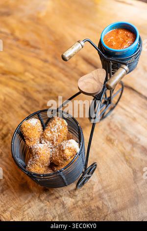 Ein dekoratives Metallfahrrad wird mit einem Korb gefüllt mit knusprigen frittierten Vorspeisen und einem kleinen Behälter mit Dippsoße präsentiert. Stockfoto