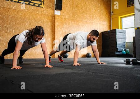 Zwei Erwachsene, die während des Fitnesstrainings Liegestütze auf einem Fitnessraum spielen Stockfoto