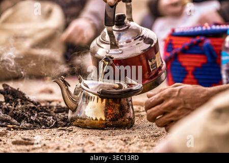 Marsa alam, ägypten 21. april 2026: Von Hand heißer Tee aus einem Wasserkocher in einen anderen gießen, umgeben von Asche nach einem Feuer, und eine alte Gastfreundschaft praktizieren Stockfoto