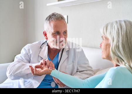 Seniorenmedizin und ärztliche Untersuchung. Ein männlicher Arzt in einem weißen Mantel und Stethoskop nimmt während einer Konsultation den Puls einer älteren Frau, p Stockfoto