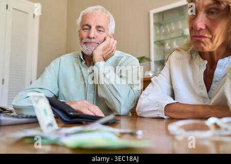 Finanzieller Stress und Herausforderungen bei der Altersvorsorge: Ein Seniorenpaar mit Geld und Taschenrechner an einem Tisch zu zeigen, das besorgt und besorgt erscheint Stockfoto