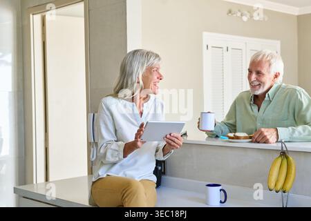 Gesundes Altern und digitale Inklusion, die ein älteres Paar zeigt, das seinen Morgenkaffee und das Frühstück in einer hellen, modernen Küche genießt. Stockfoto